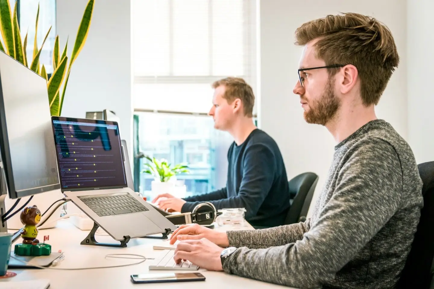 Two employees at desks with laptop and monitor – devices kept updated and monitored