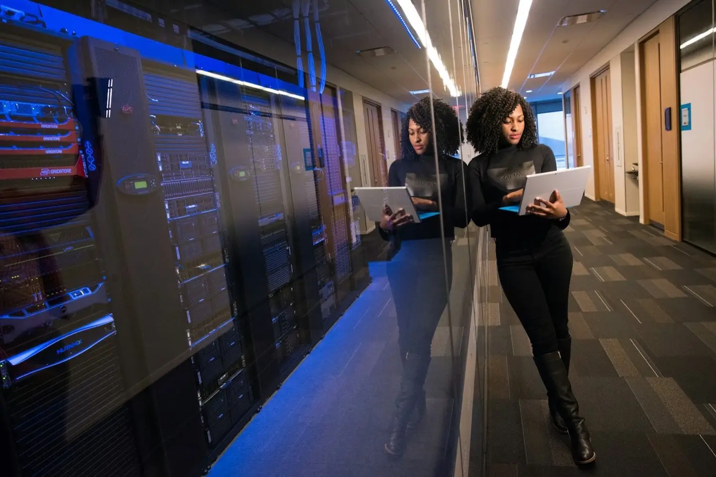 IT specialist with a tablet in front of a glass-walled server room – IT operations for mid-sized companies